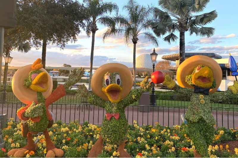 Three Caballeros Topiaries at Mexico Pavilion - Epcot Flower and Garden Festival 2022 with sunset and Spaceship Earth in the background