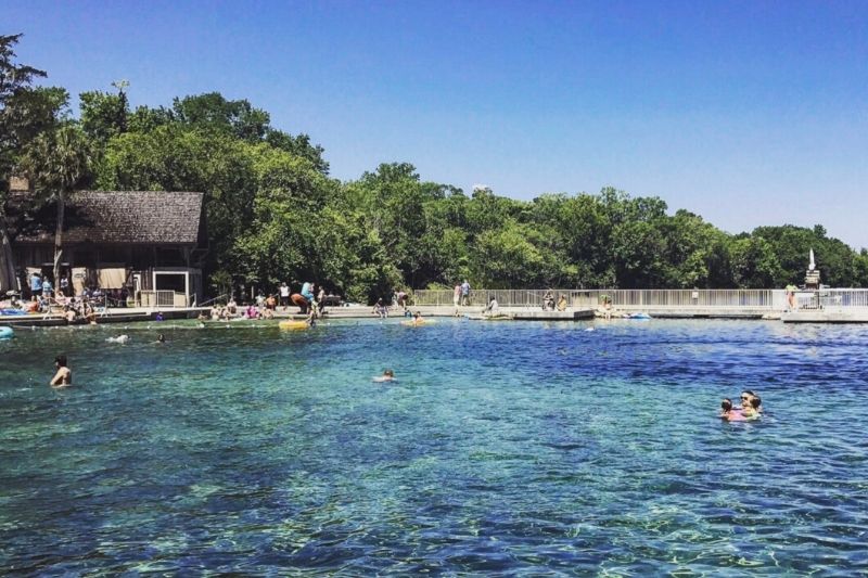 Swimming at De Leon Springs State Park with blue skies and sparkling water, Sugar Mill restaurant in the background