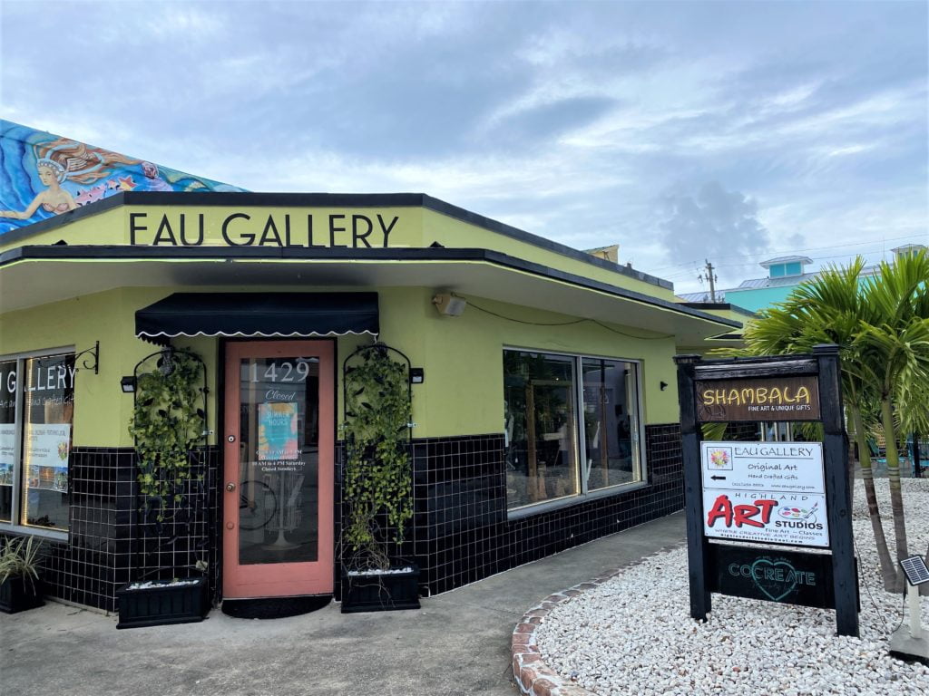 EAU Gallery in the Eau Galle Arts District - Melbourne, Florida has a pale yellow facade with shiny black tile along the bottom portion on the building. 