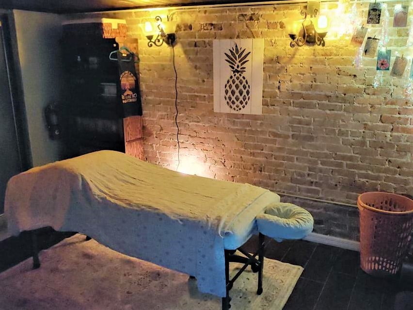5D Serenity Wellness Studio Massage Room features historic brick walls, soft warm lighting, a welcoming massage table with white sheets, and positive affirmations as decorations