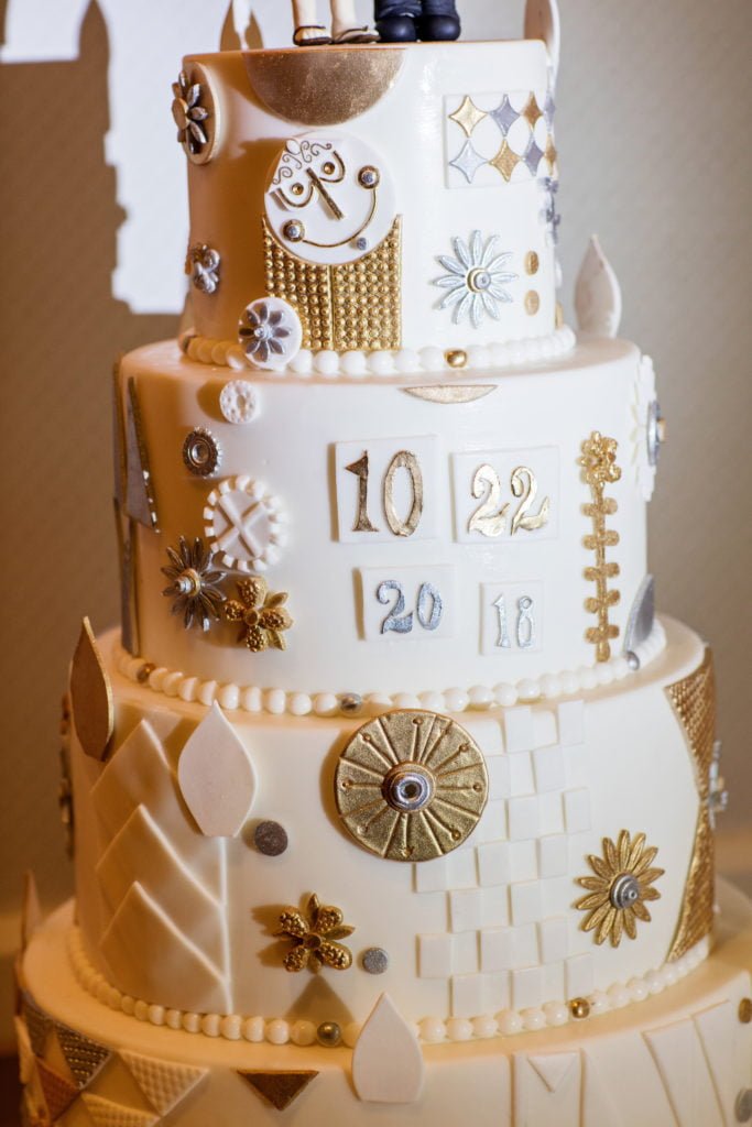 “it’s a small world” inspired cake features classic designs and colors from the final room of the classic Magic Kingdom attraction. (Disney) with three tiers and white, gold, and silver adornments