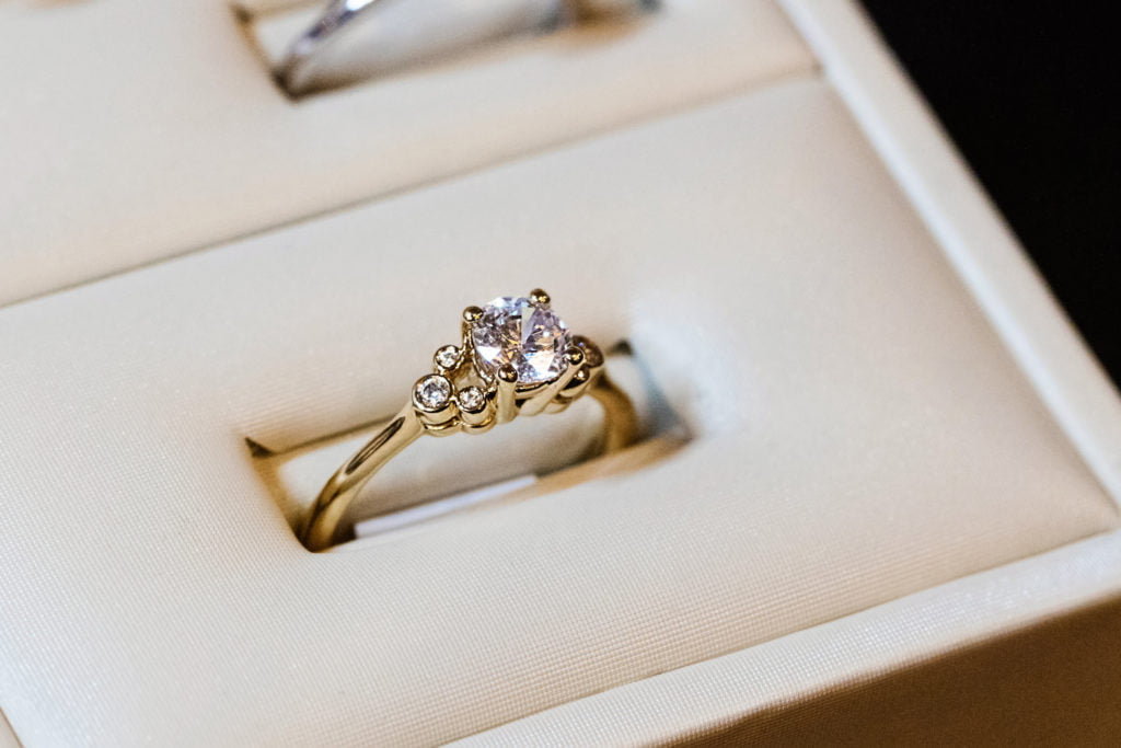 A Disney engagement ring with a heartshaped diamond and smaller diamonds, and a gold band sits in a white ring holder box