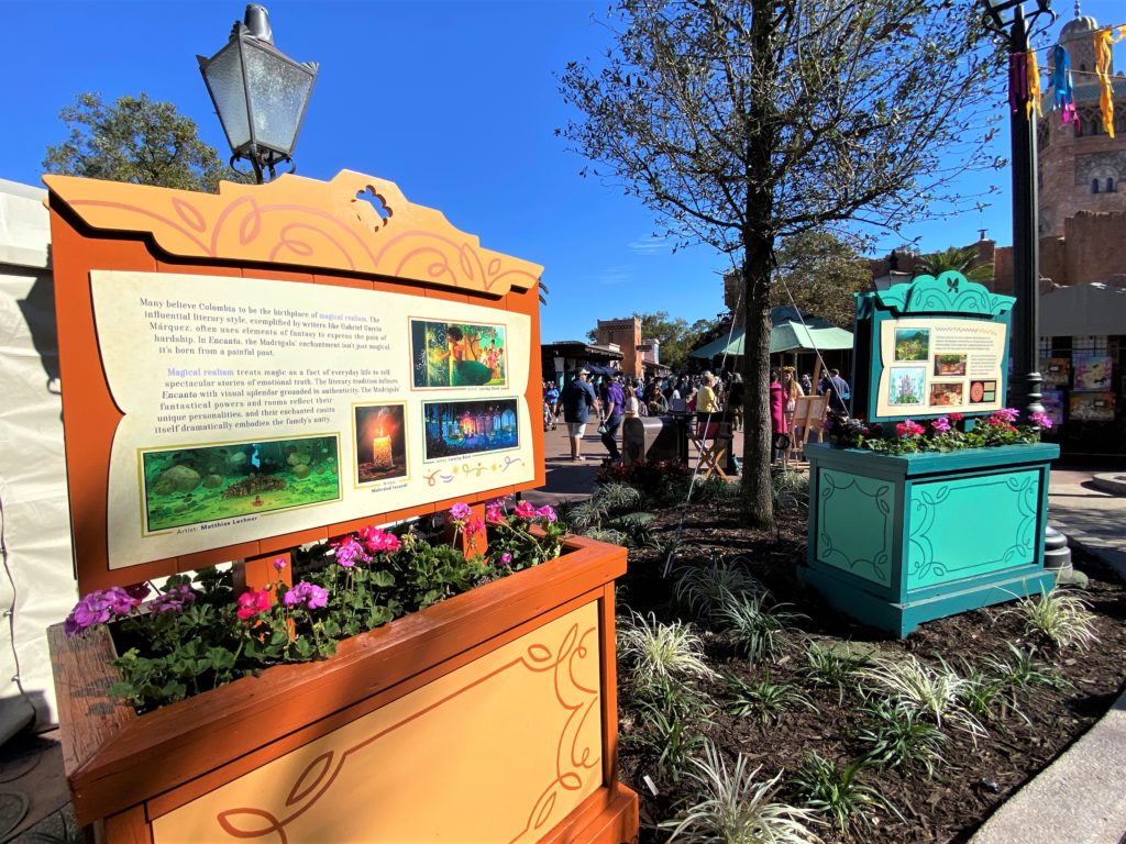 Encanto Concept Art and Info at Epcot Art Festival is on display on horizontal signs inside flower boxes, with bold colors like teal and terra cotta