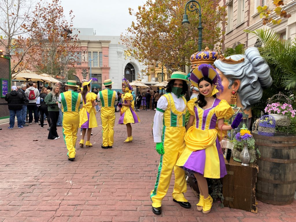 Universal Mardi Gras 2022 New York Area Food Booths and Performers pose for a photo while wearing bright yellow, purple, and green costumes