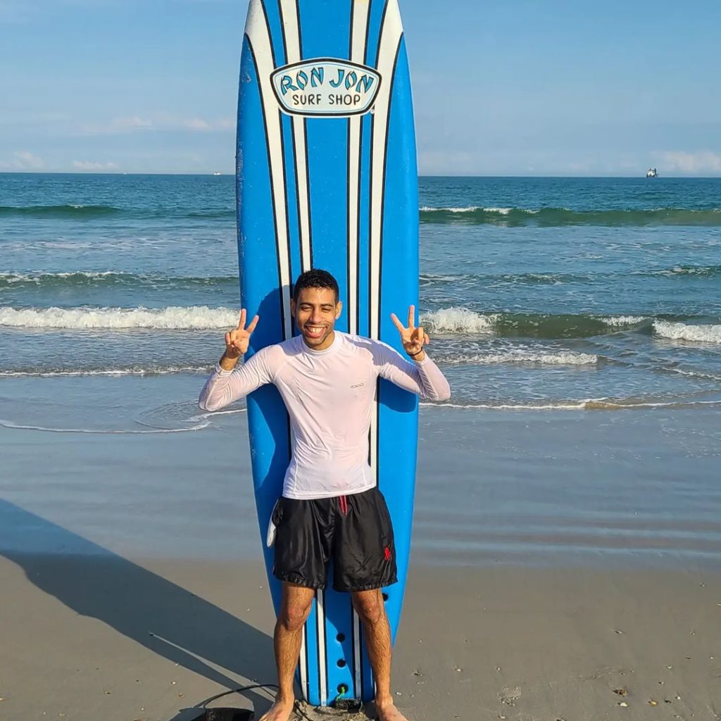 A young man stands in front of a surfboard on Cocoa Beach