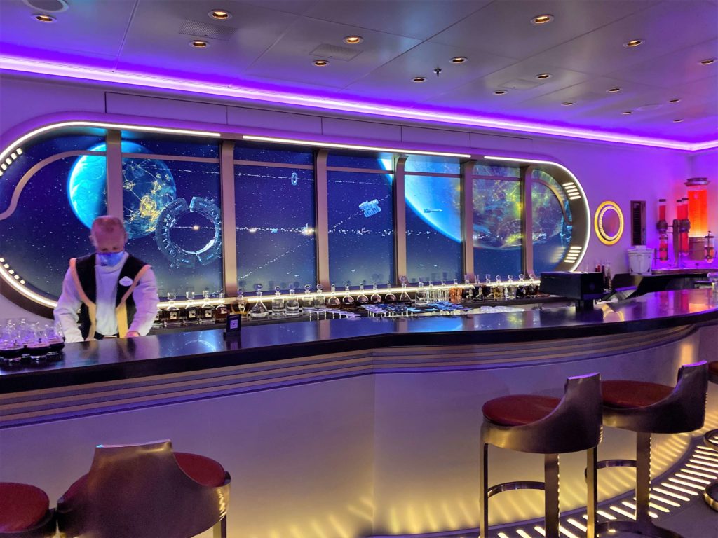 Looking at the bar with video screen showing star wars ships and planets at Star Wars Hyperspace Lounge on Disney Wish